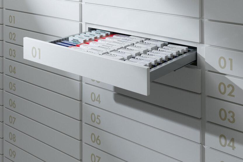 Detailaufnahme von schmalen weißen Medikamentenschubläden mit dezenter Nummerierung und sichtbarer Medikamentenaufteilungen.